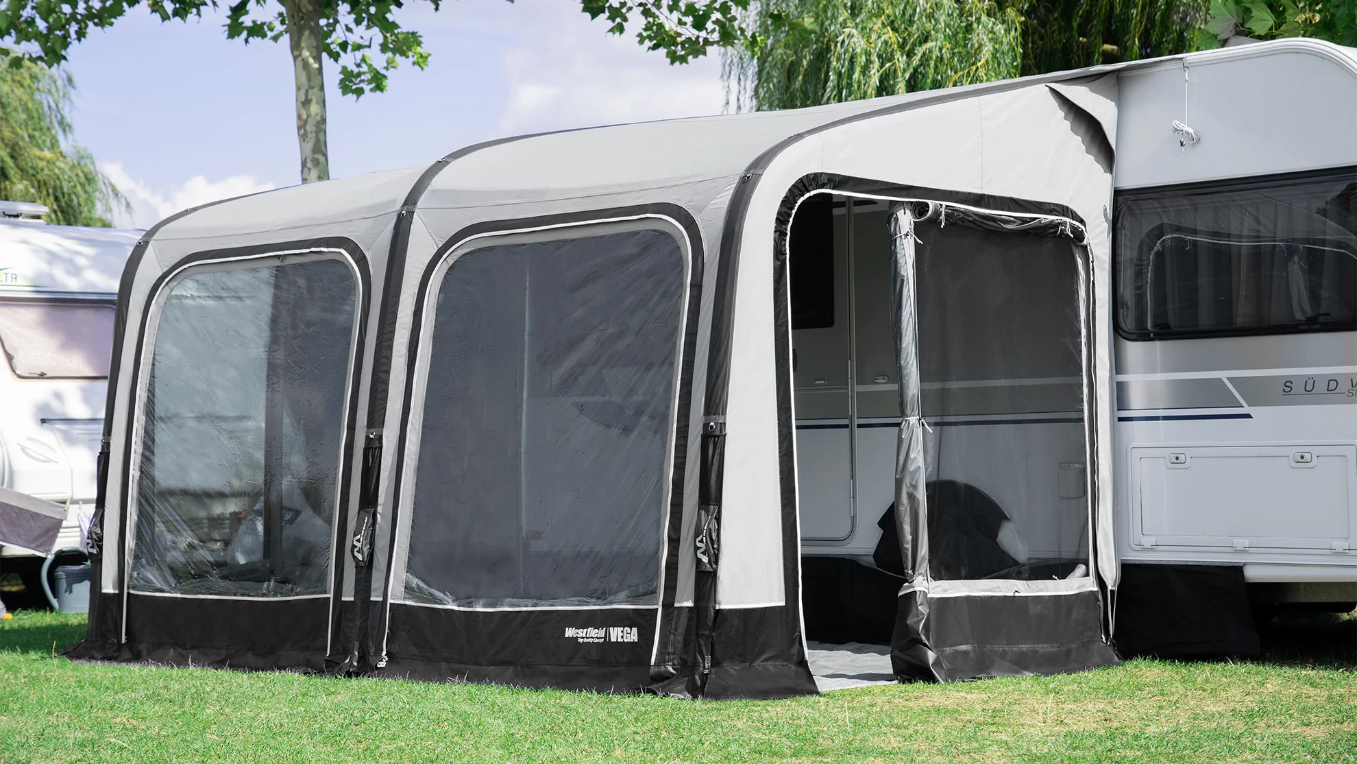 Wohnwagen mit angebautem Vorzelt auf Rasenplatz.