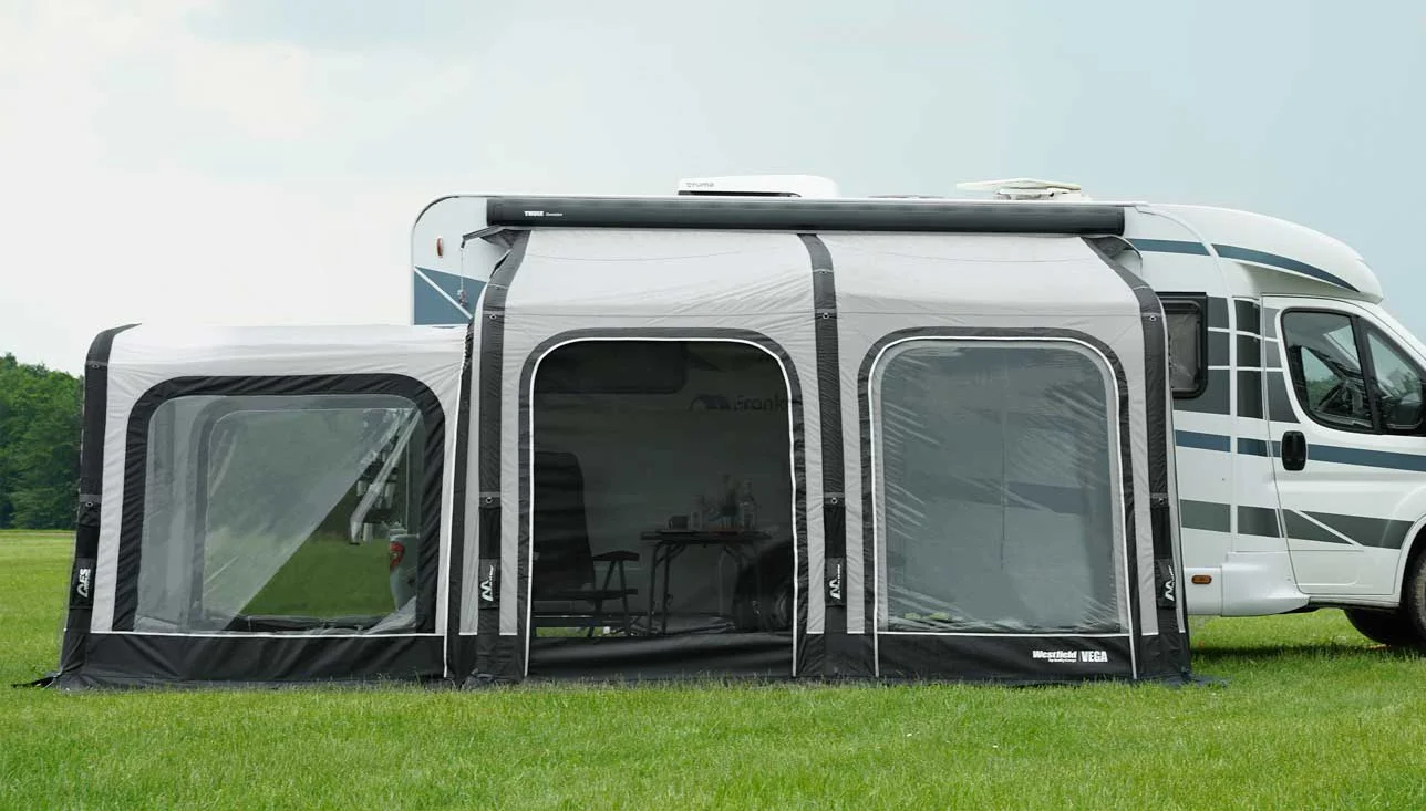 Wohnmobil mit Vorzelt auf grüner Wiese.