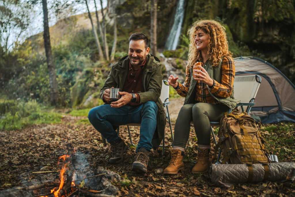 Zwei Personen campen am Lagerfeuer im Wald.